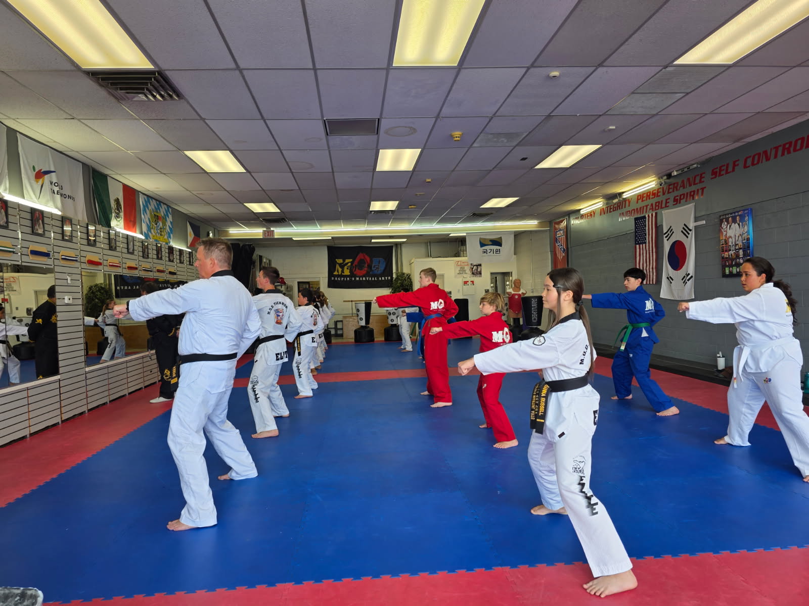 Students holding stances through drills during a class at MOD Taekwondo Roy, with instructors watching from the front of the mat