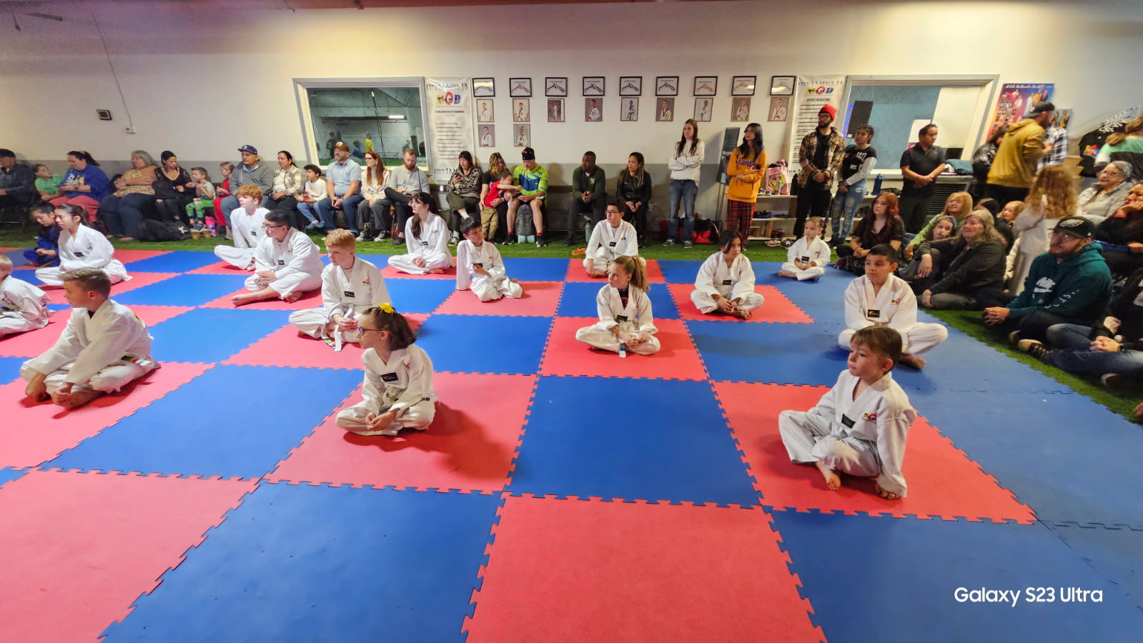 Students seated on the mats during a belt testing event at MOD Taekwondo North Ogden with parents watching from the sidelines