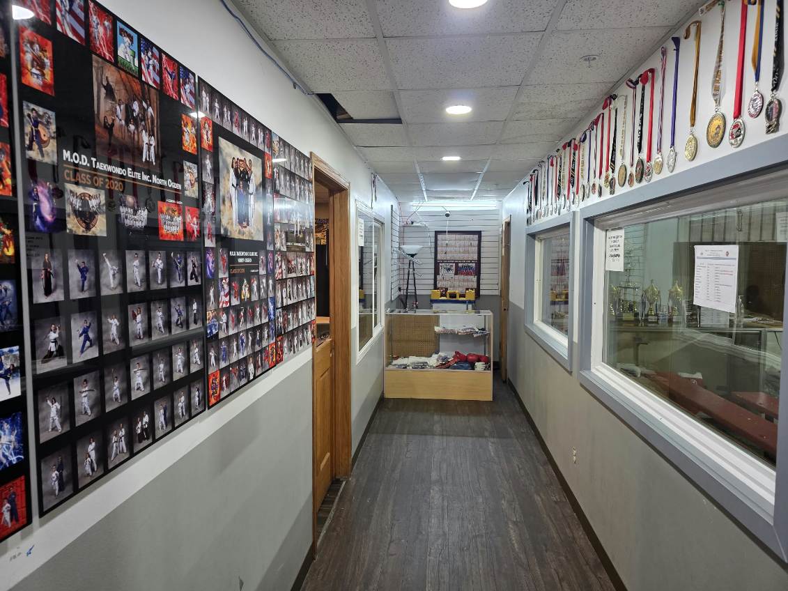 Hallway at MOD Taekwondo North Ogden lined with class photos, medals, and trophy displays